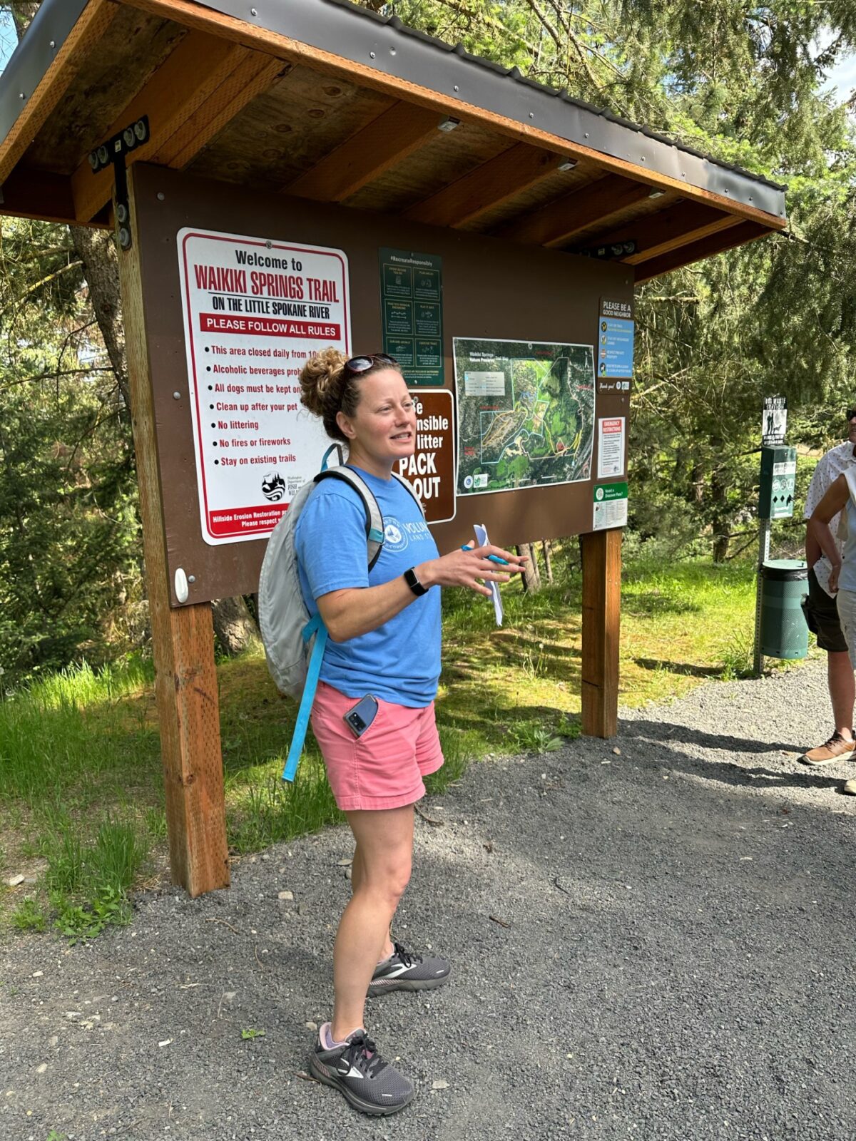Hike docent Alana Livingston standing in front of trail head kiosk at Waikiki Springs